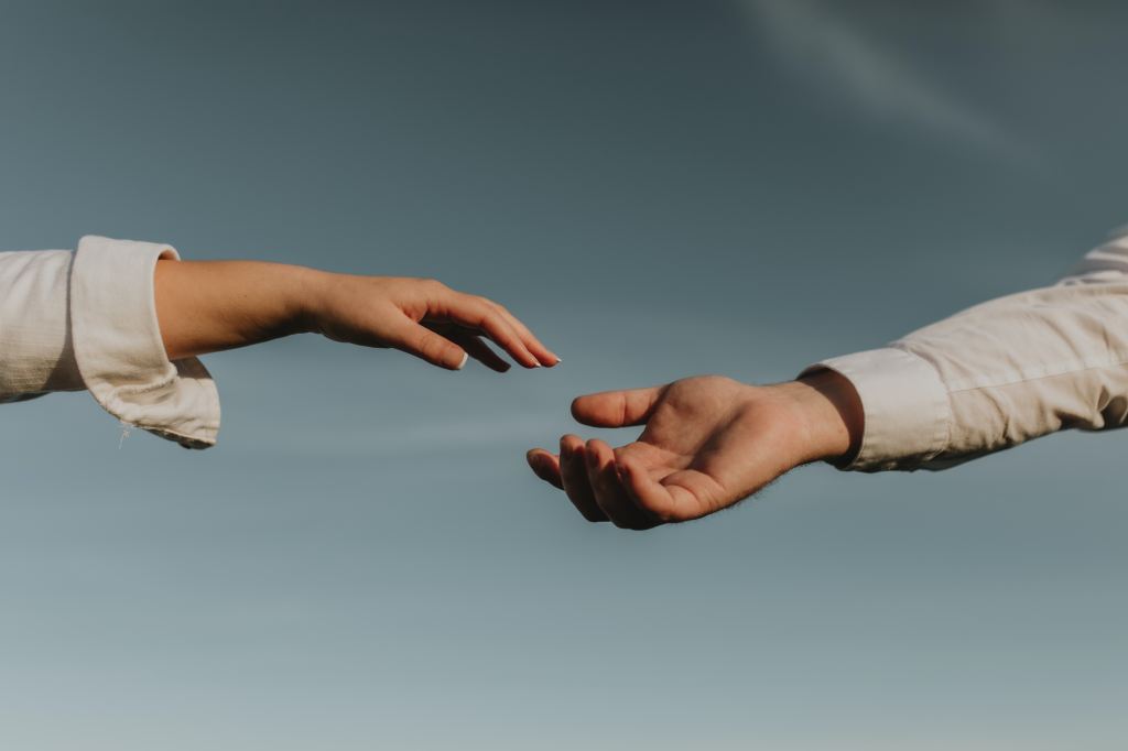 Two hands reaching toward each other against a pale blue sky