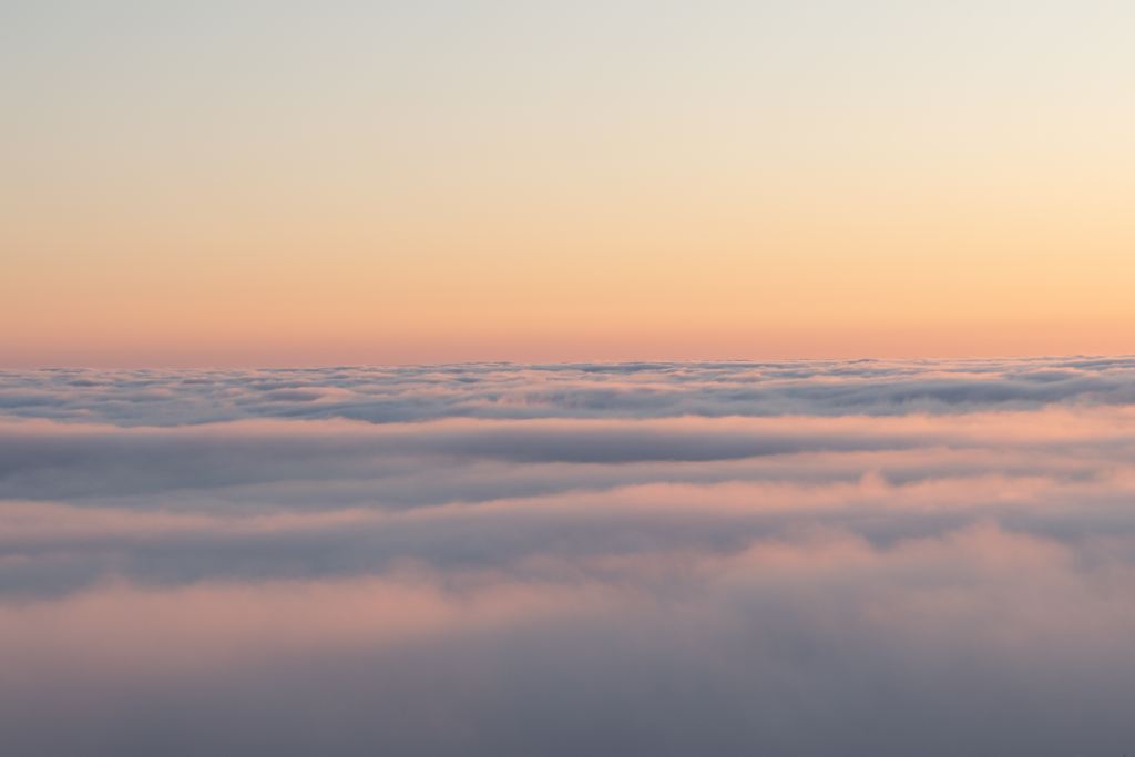 A sea of clouds under a soft pink and orange sky