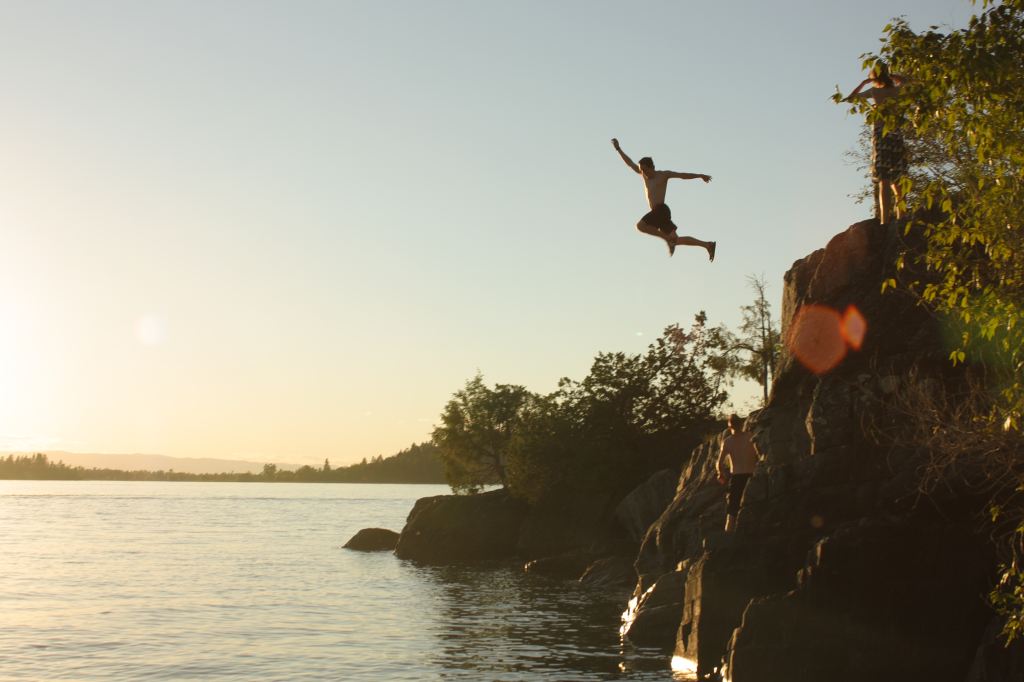 A person leaping from a rocky ledge into a lake at sunset