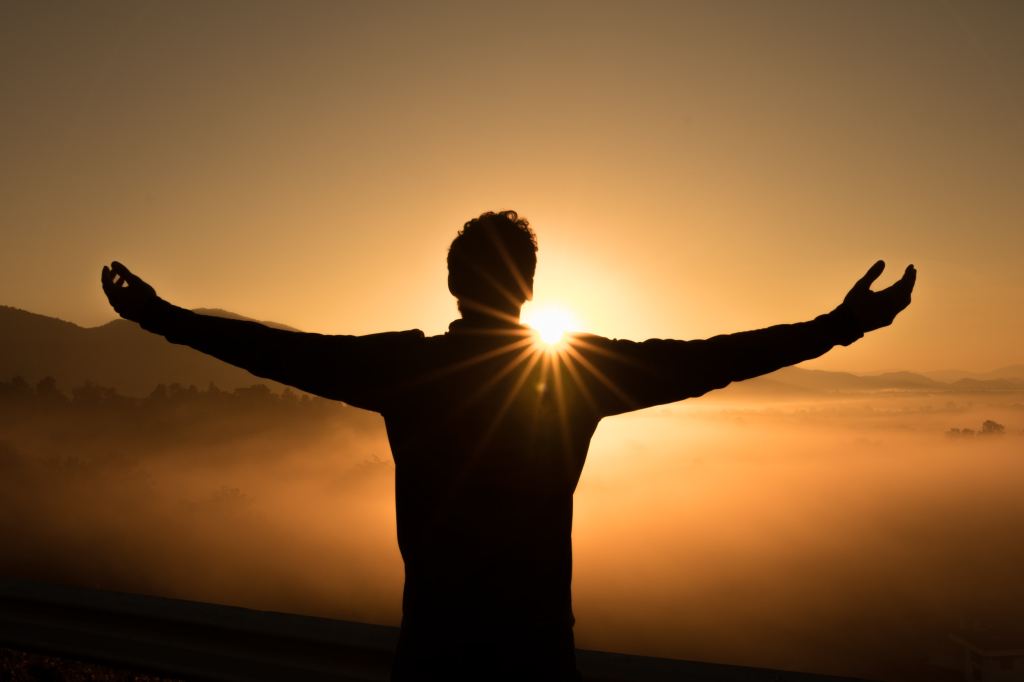 A man silhouetted with arms spread wide against a golden sunrise