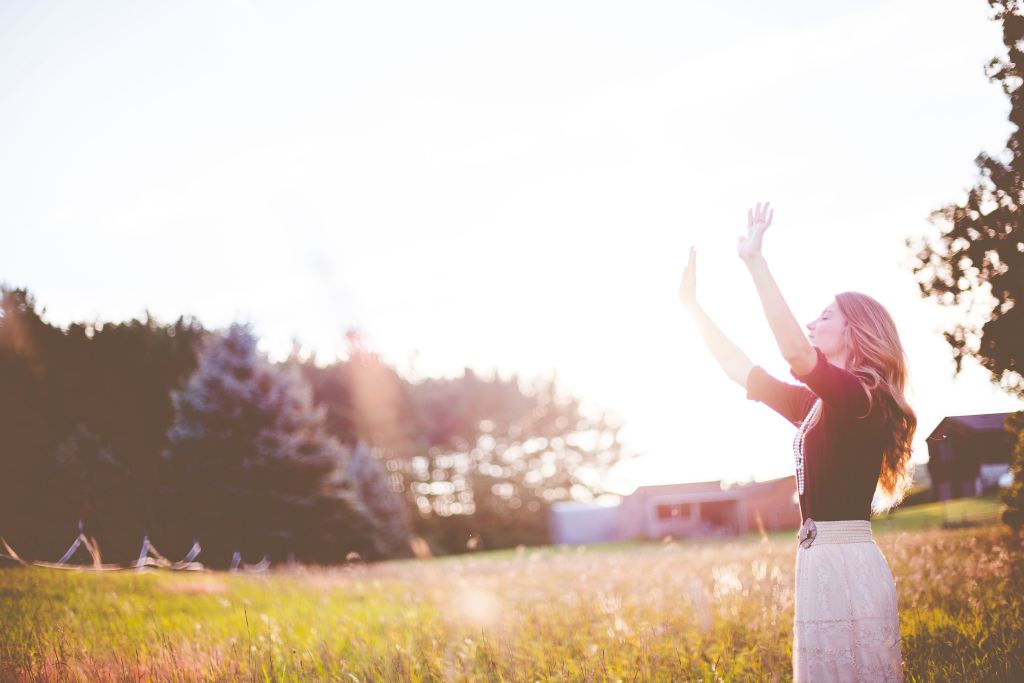 A woman raising her hands toward the sun in a bright, grassy field
